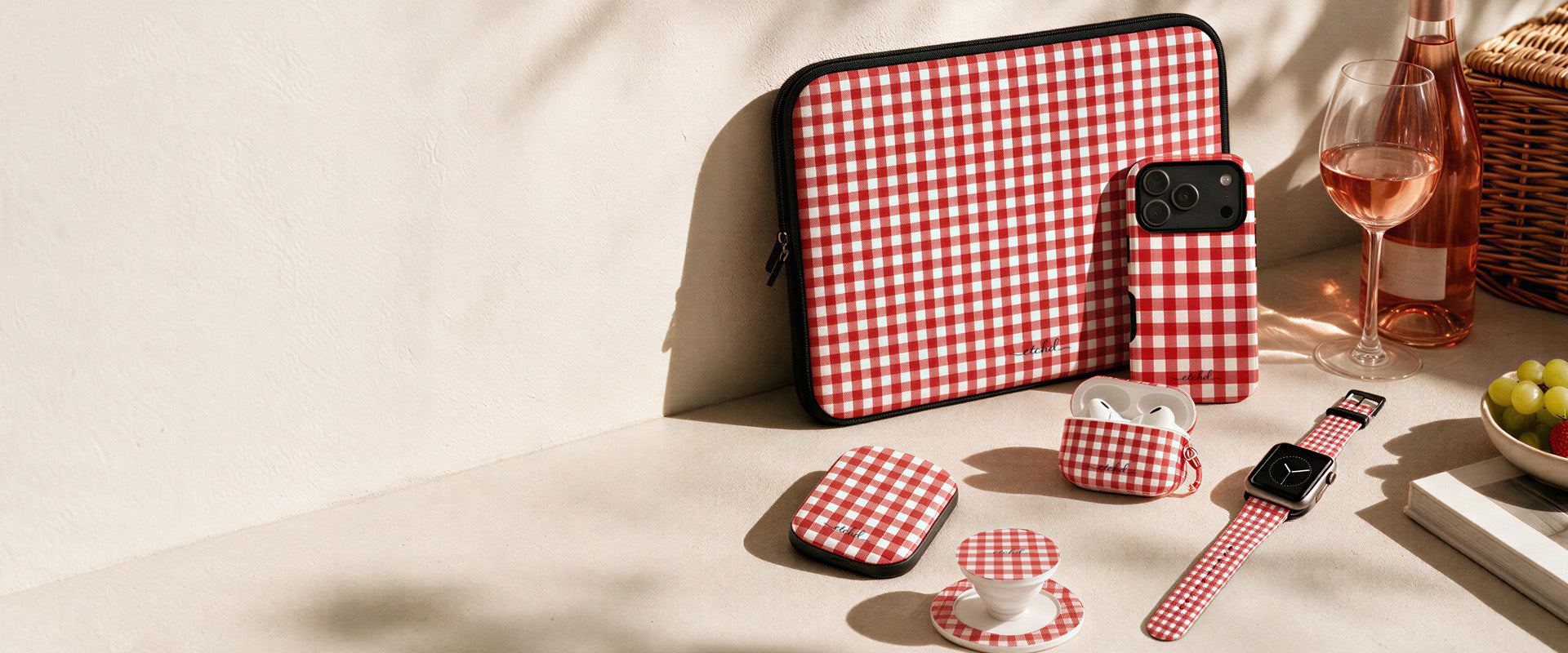 Red gingham laptop sleeve, phone case, power bank, AirPod case, phone grip and watch strap by etchd set out for a picnic