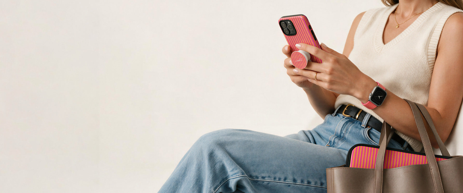 Woman holding a pink striped phone case by etchd with a matching phone grip, watch strap and laptop sleeve in her tote